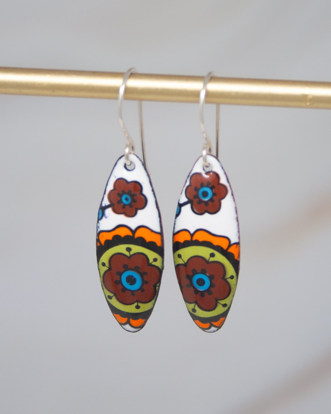 A pair of colorful earrings with floral designs hanging from a gold-colored metal hook.