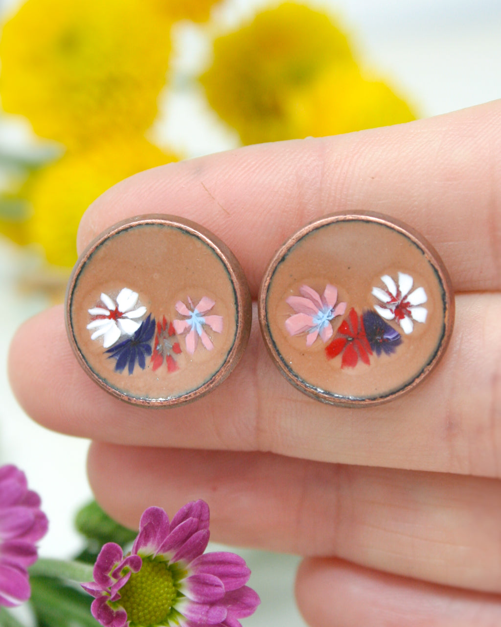 a hand holding a pair of earrings with flowers on them