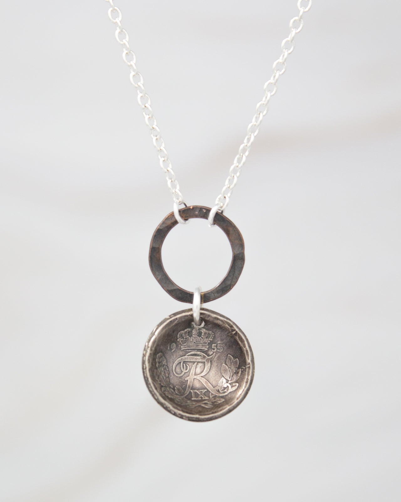 A silver necklace with a round pendant featuring an engraved letter "R" on it.
