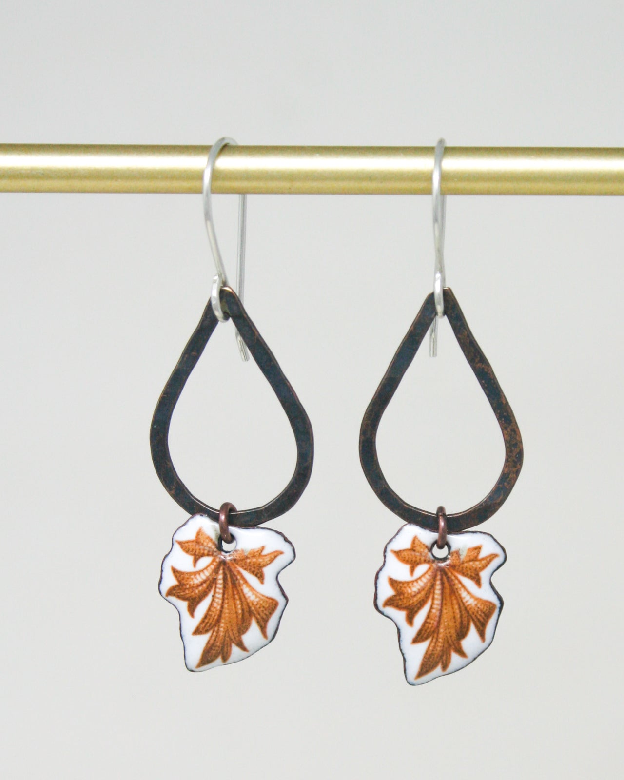 A pair of earrings with leaf-shaped pendants hanging from a gold-colored metal hook.