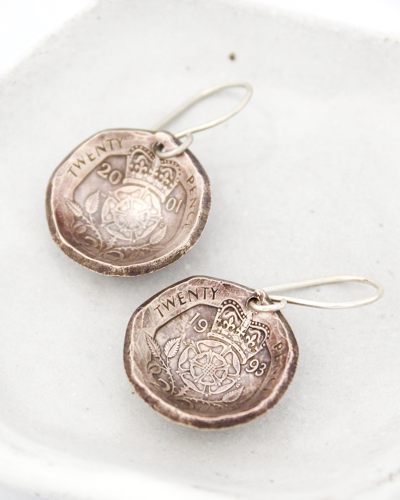 Two silver earrings made from a 20 pence coin, featuring intricate designs and the word "TWENTY" engraved on them.