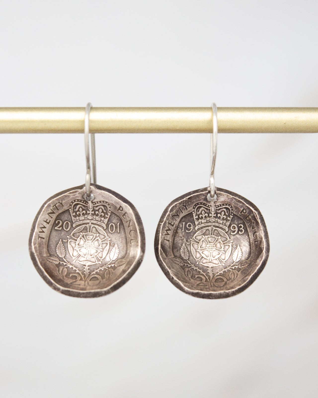 A pair of silver earrings made from a 20-pence coin, featuring the year 1993 and the year 2001 engraved on them.