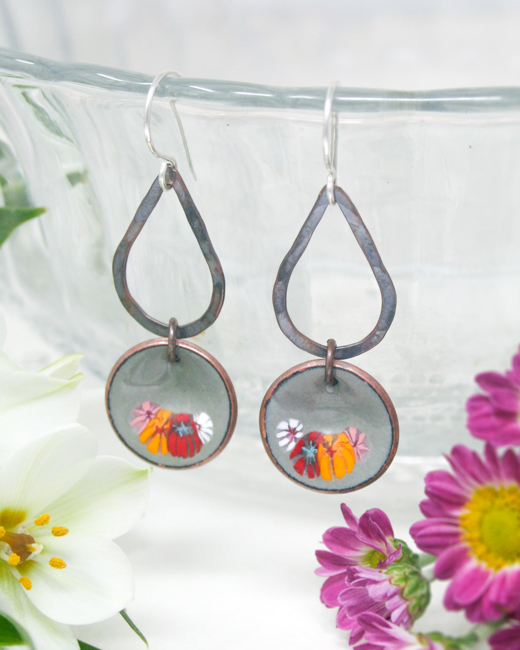 a close up of a pair of earrings with flowers in the background