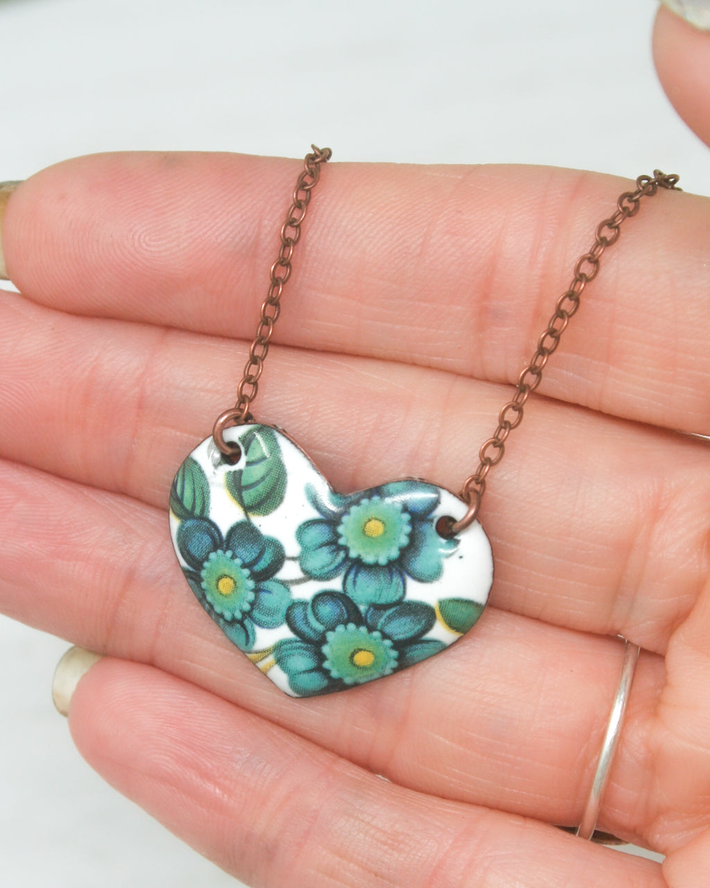 a hand holding a heart shaped necklace with flowers on it