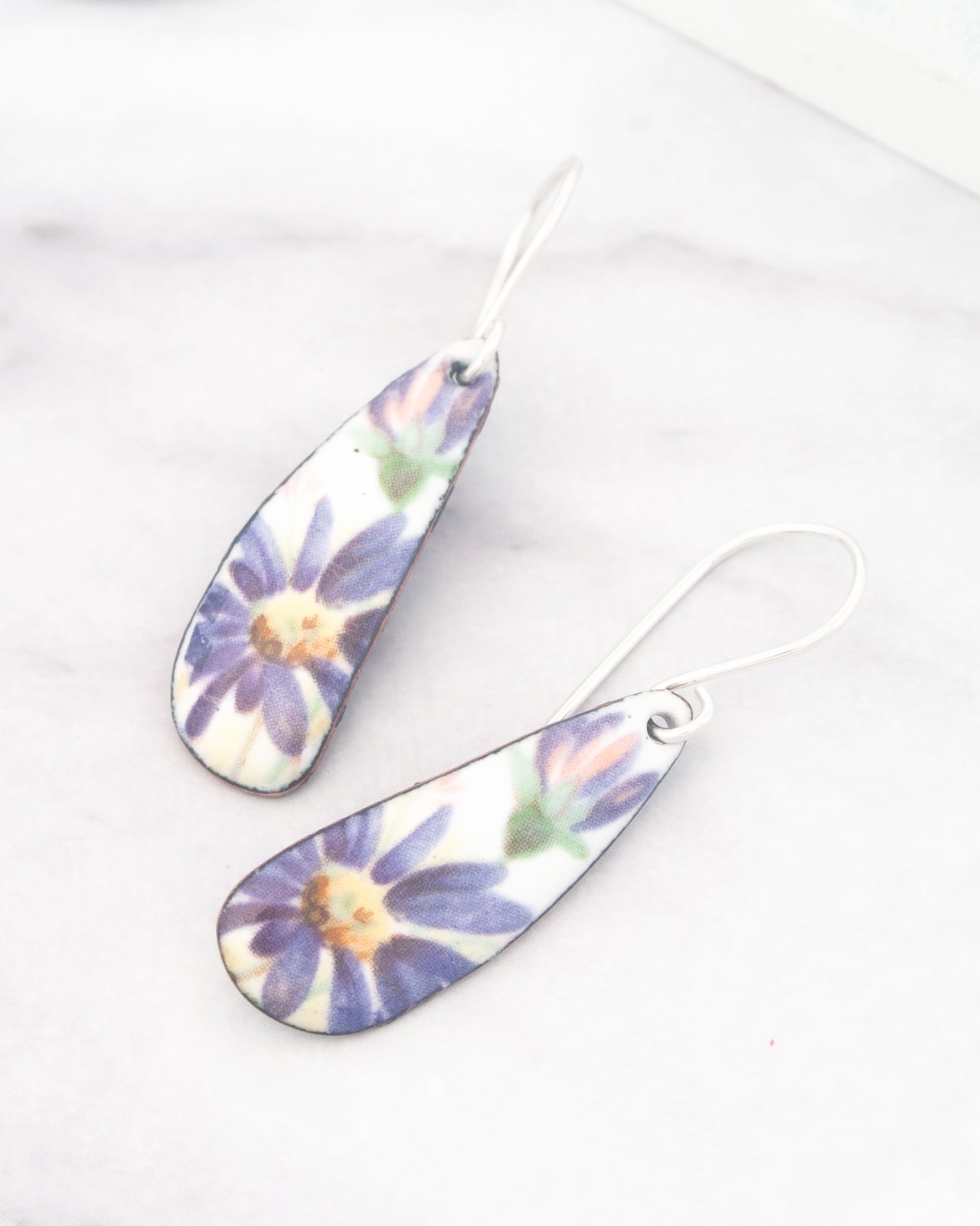 A pair of earrings with a floral design, featuring two curved pendants with purple and yellow flowers.