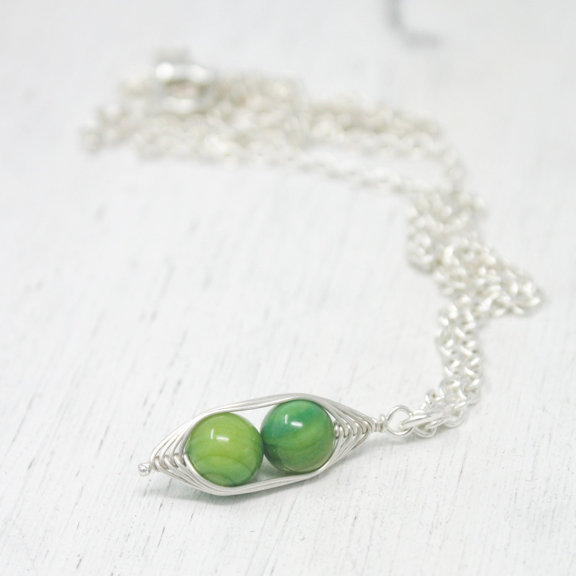 two green beads are attached to a silver chain