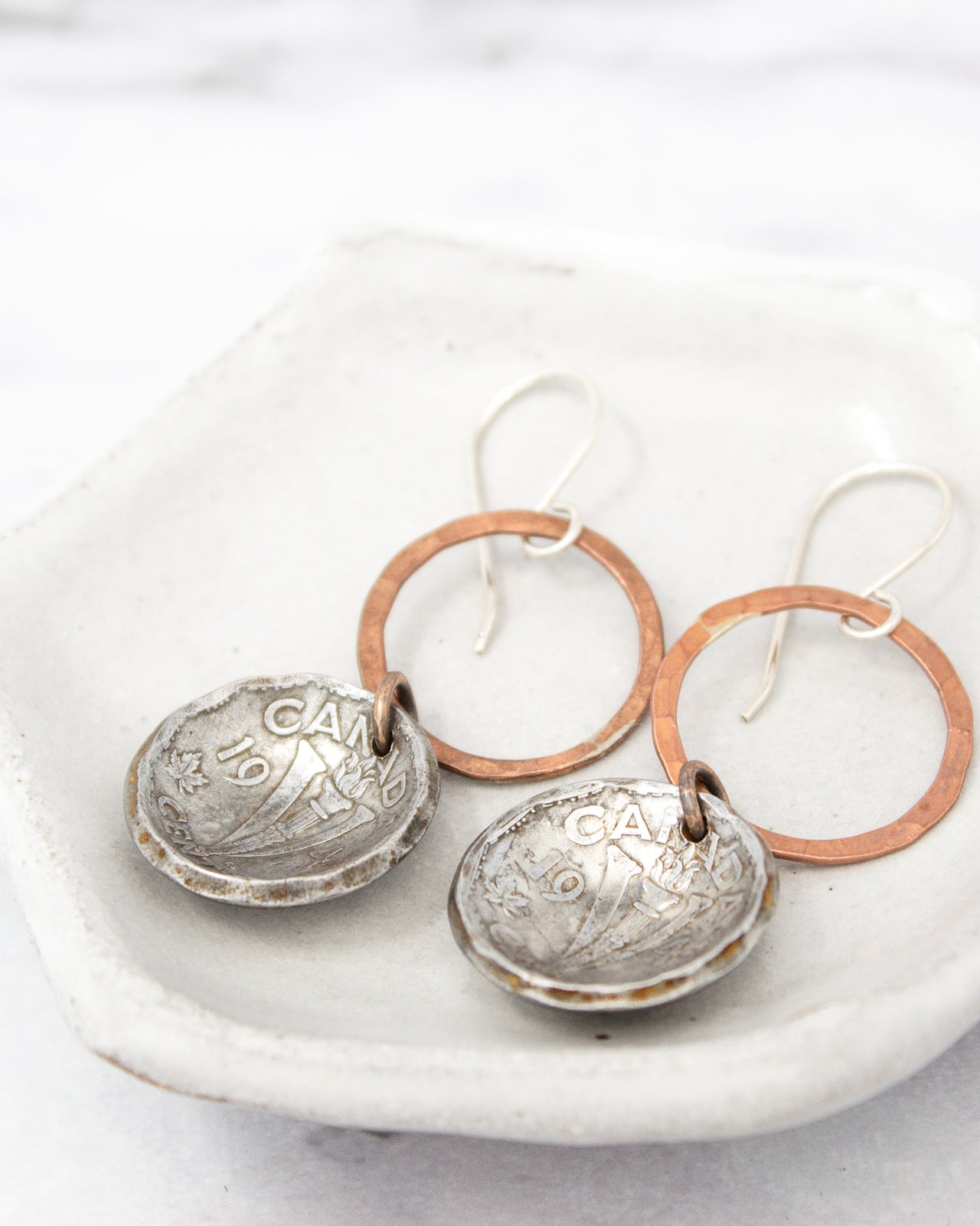 A pair of earrings with a silver and copper design, resting on a white surface.