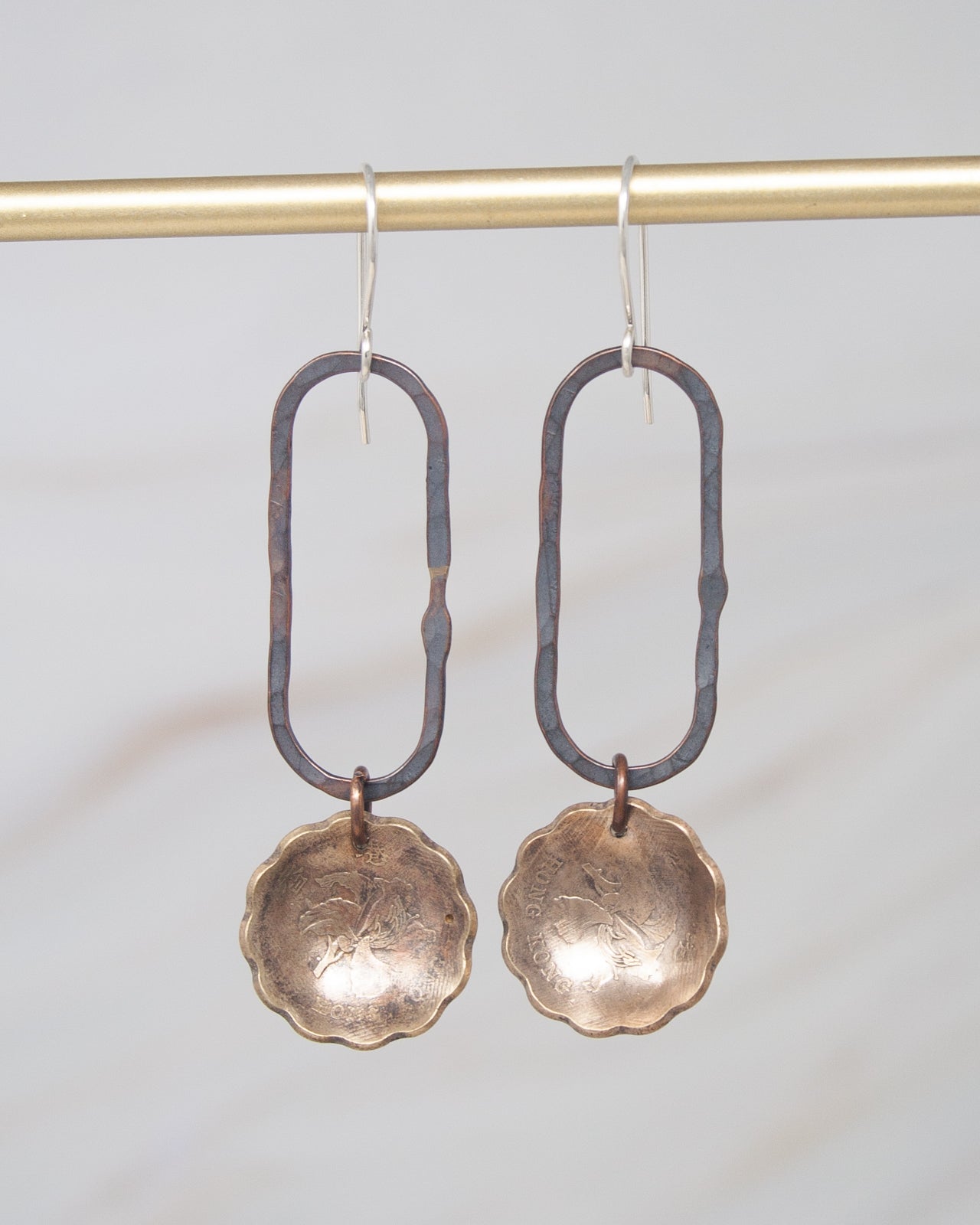 A pair of earrings with a metal frame and a round metal pendant hanging from a hook.