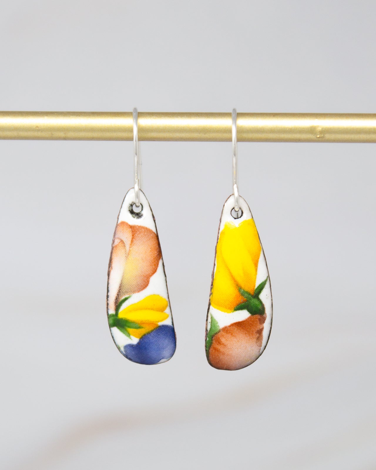 two earrings hanging from a gold bar, each with a unique floral design.