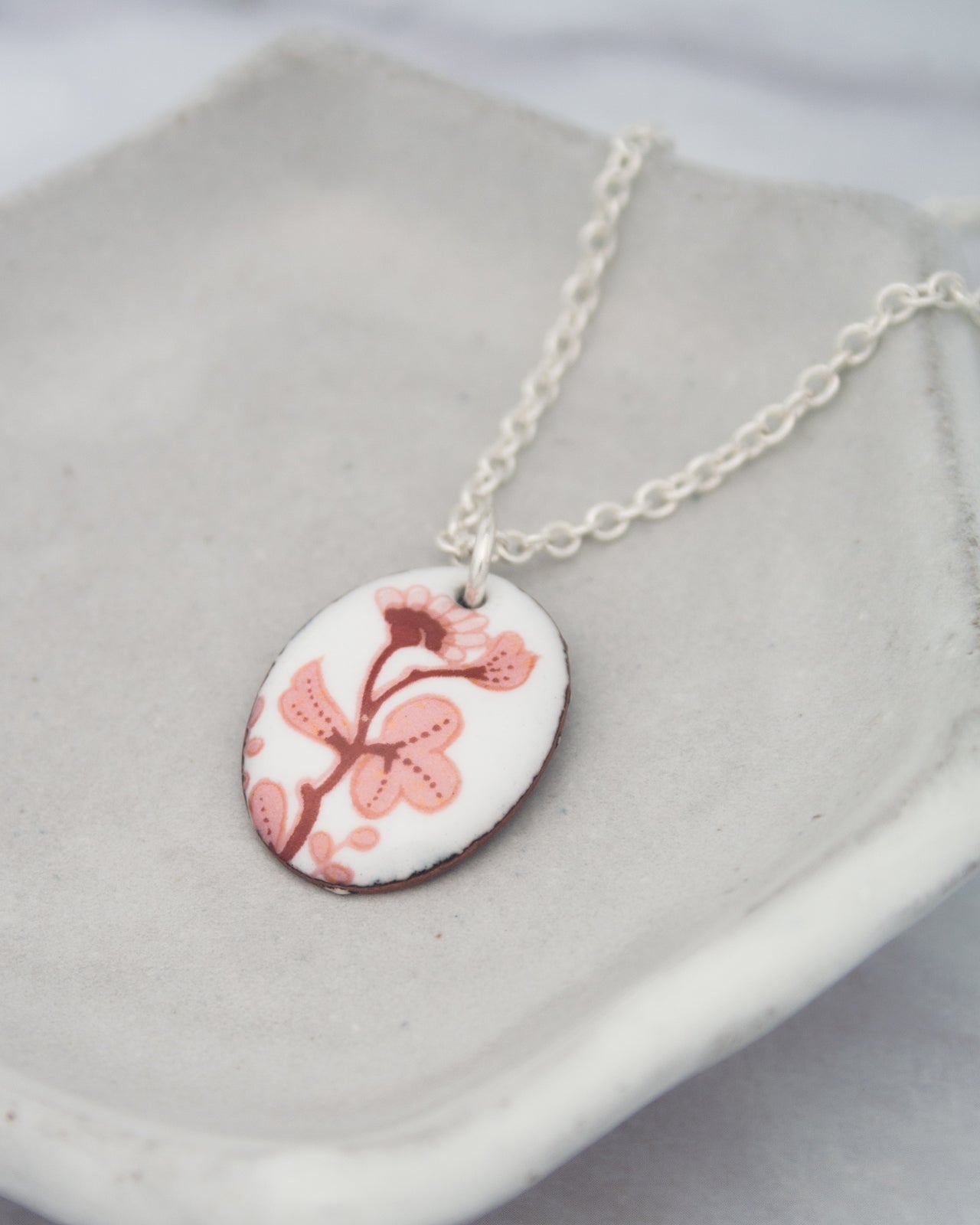 A necklace with a pendant featuring a floral design in pink and white colors.