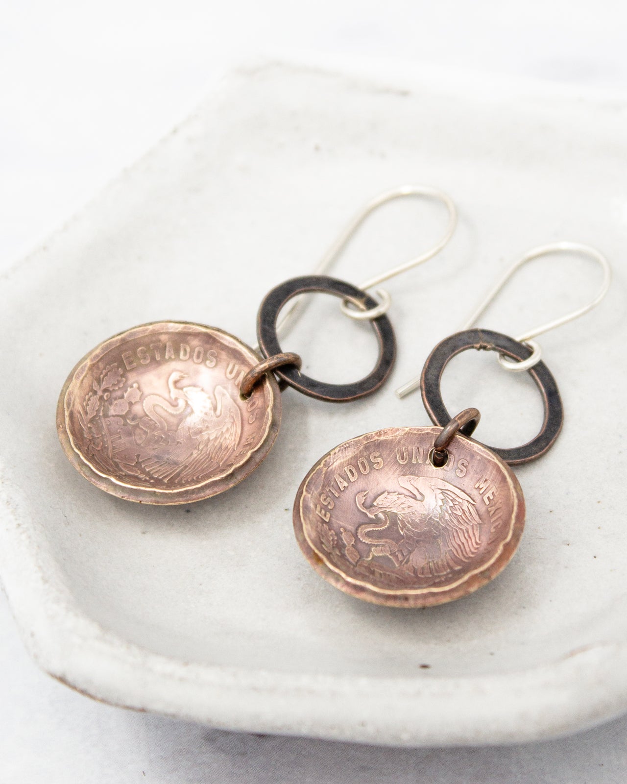 A pair of earrings made of copper-colored metal, featuring a circular design with a textured surface and a metallic ring.