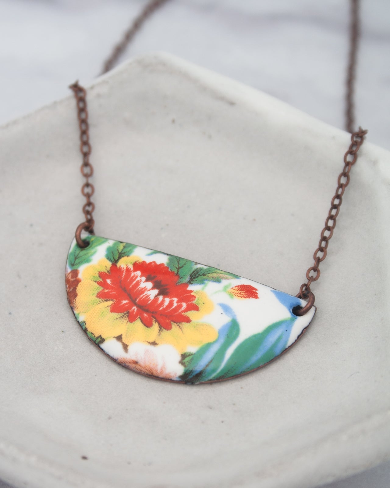 A colorful pendant necklace with a floral design on a white plate.