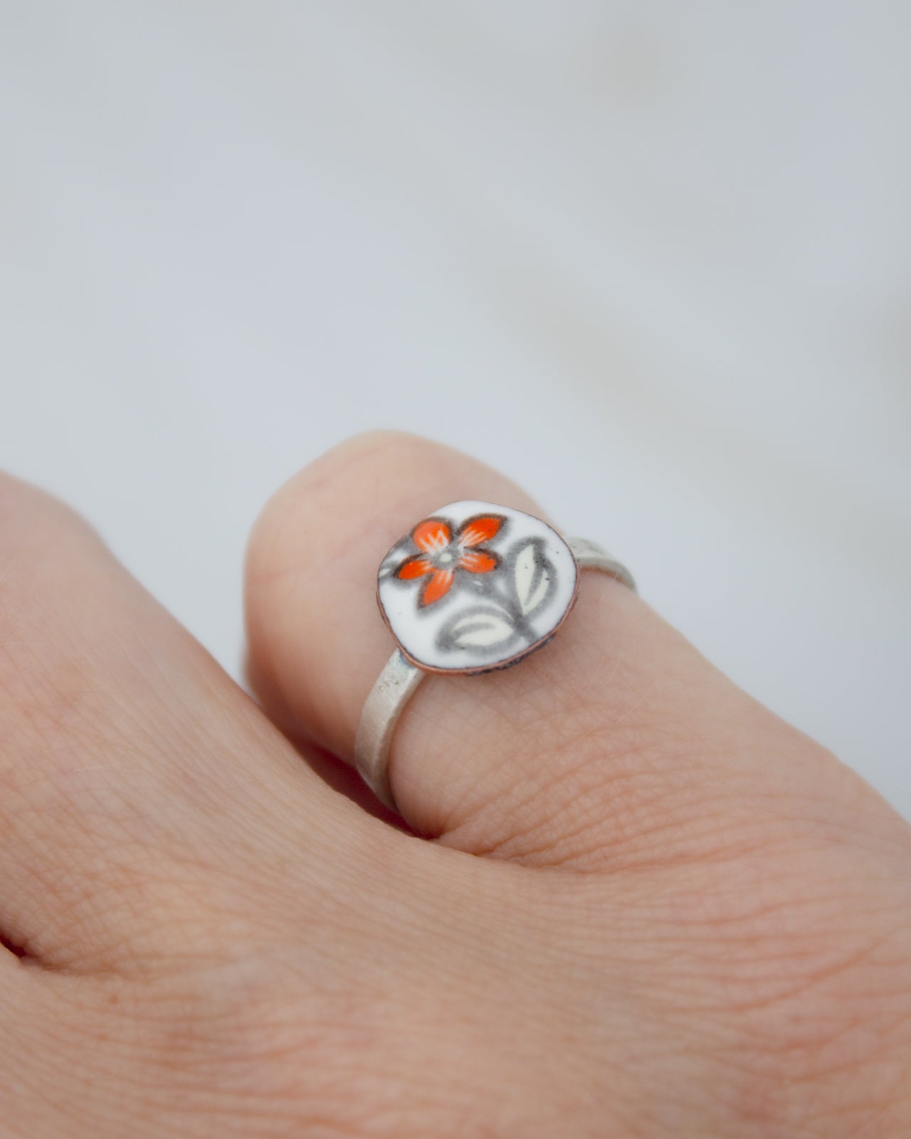 A close-up of a person's hand wearing a ring with a small flower design on it.