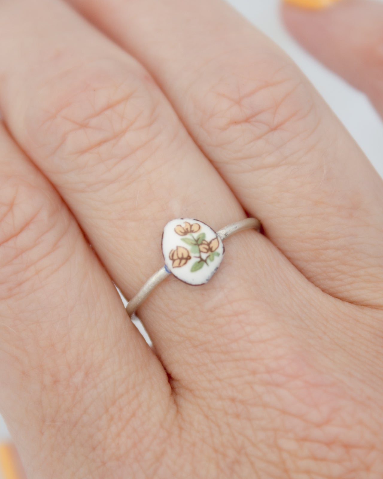 A close-up of a person's hand wearing a ring with a small floral design on it.