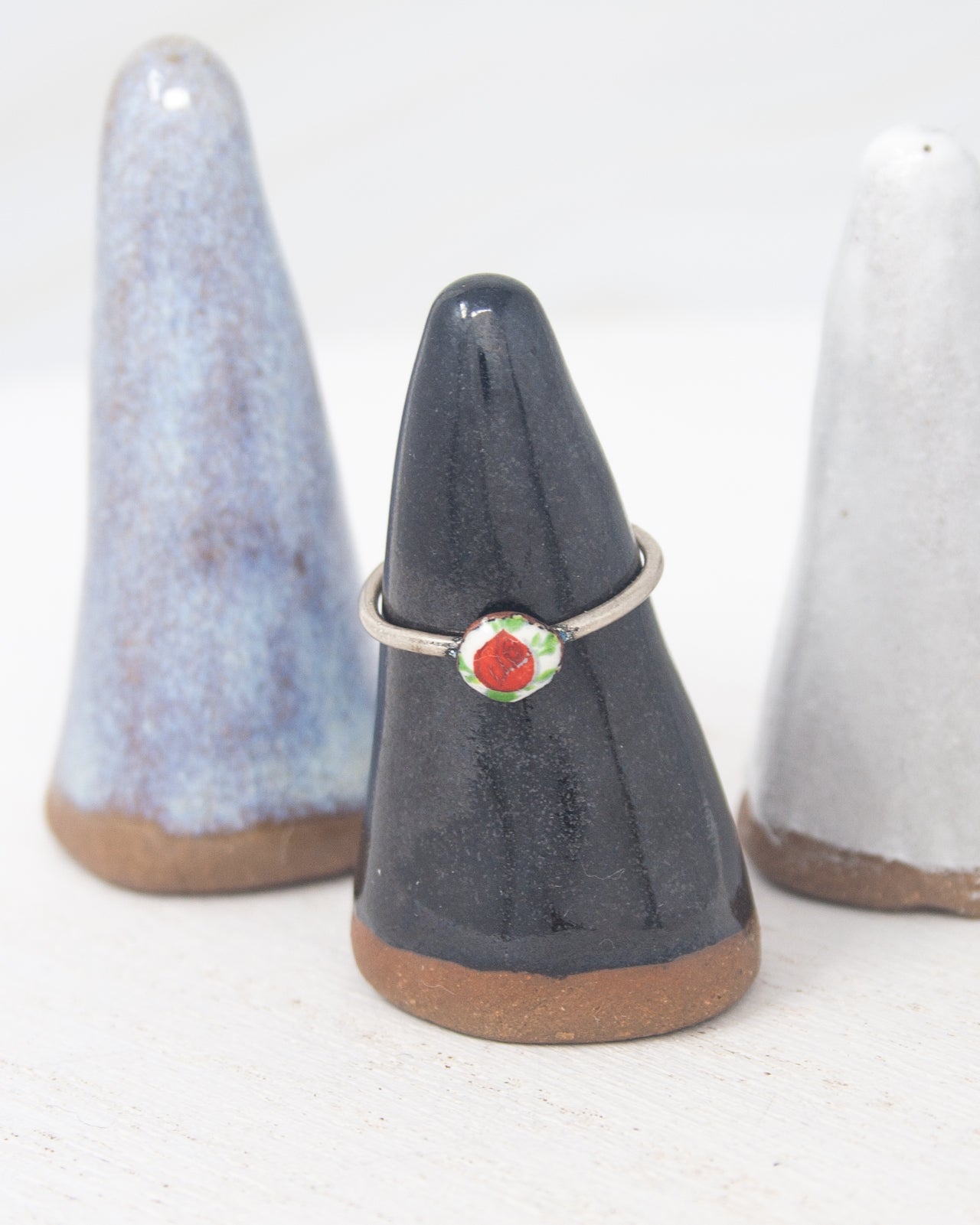 A ring is displayed on a black ceramic stand, with a white ceramic stand to the left and a white ceramic stand to the right.