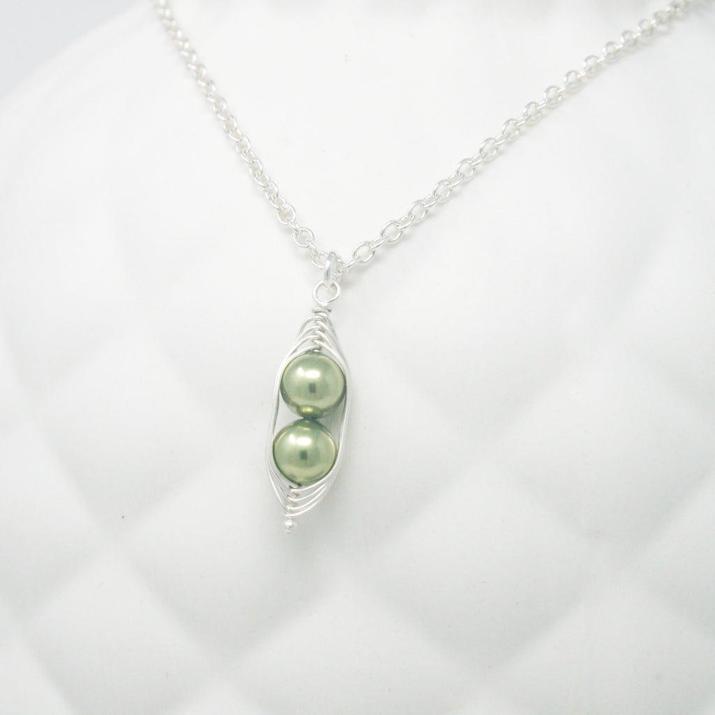 a close up of a necklace with two peas on it