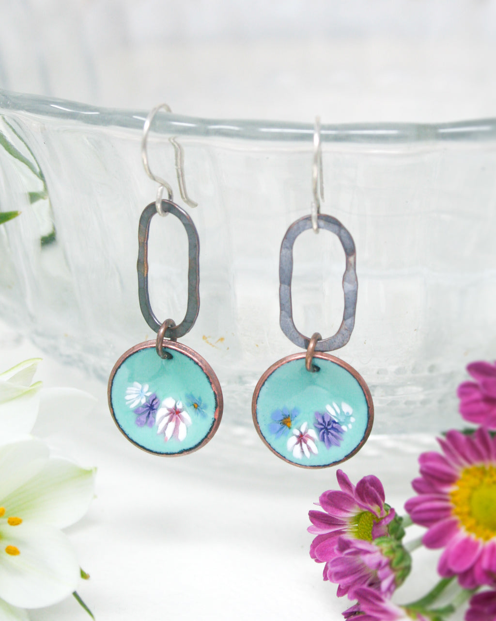 a close up of a pair of earrings with flowers in the background