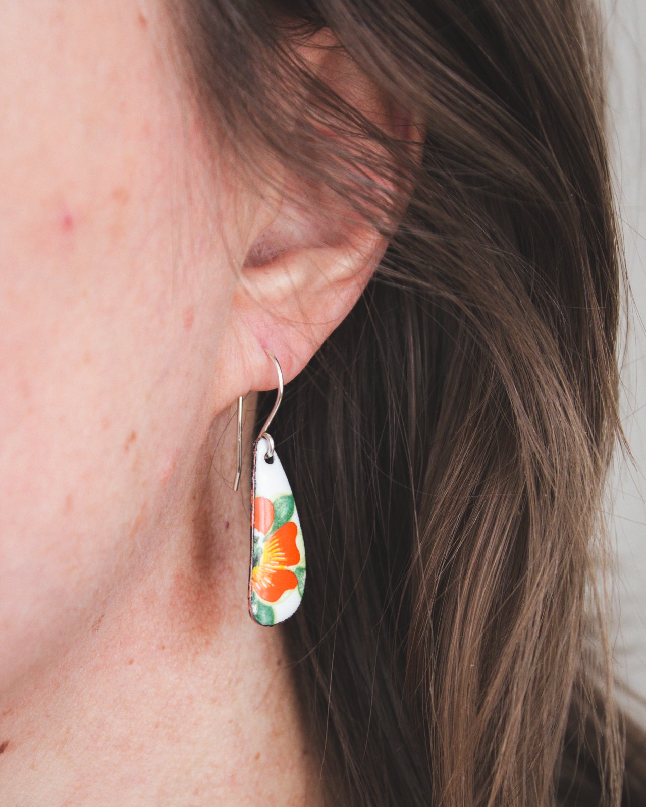 A close-up view of a person's ear wearing a pair of earrings with a floral design.