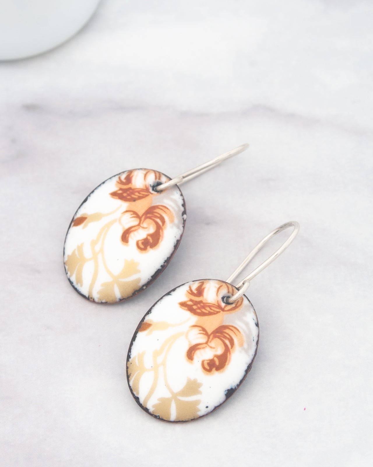 A pair of earrings with a floral design on a white marble surface.