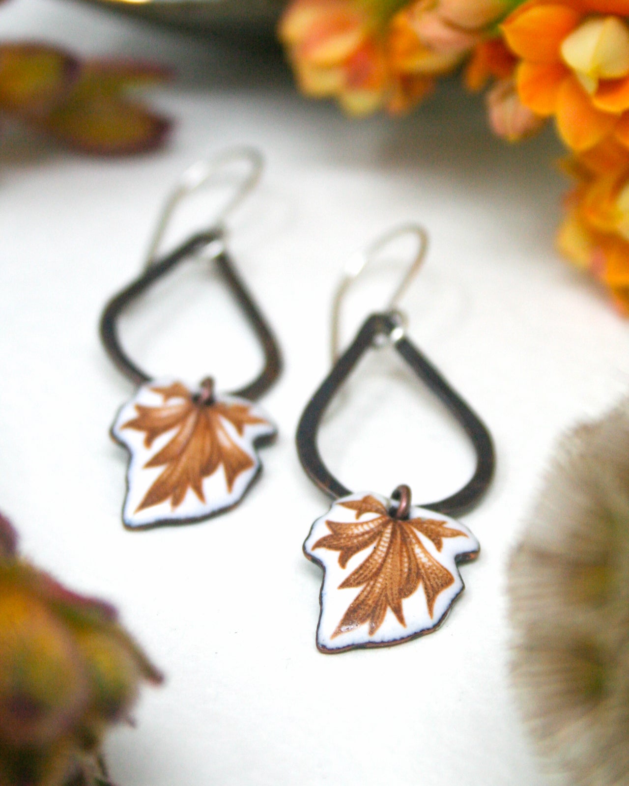 A pair of earrings with leaf-shaped pendants, featuring a combination of black and white colors, are displayed on a white surface.