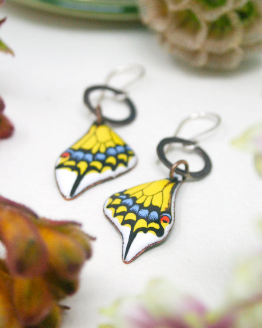 a pair of colorful butterfly-shaped earrings with intricate designs, placed on a white surface.