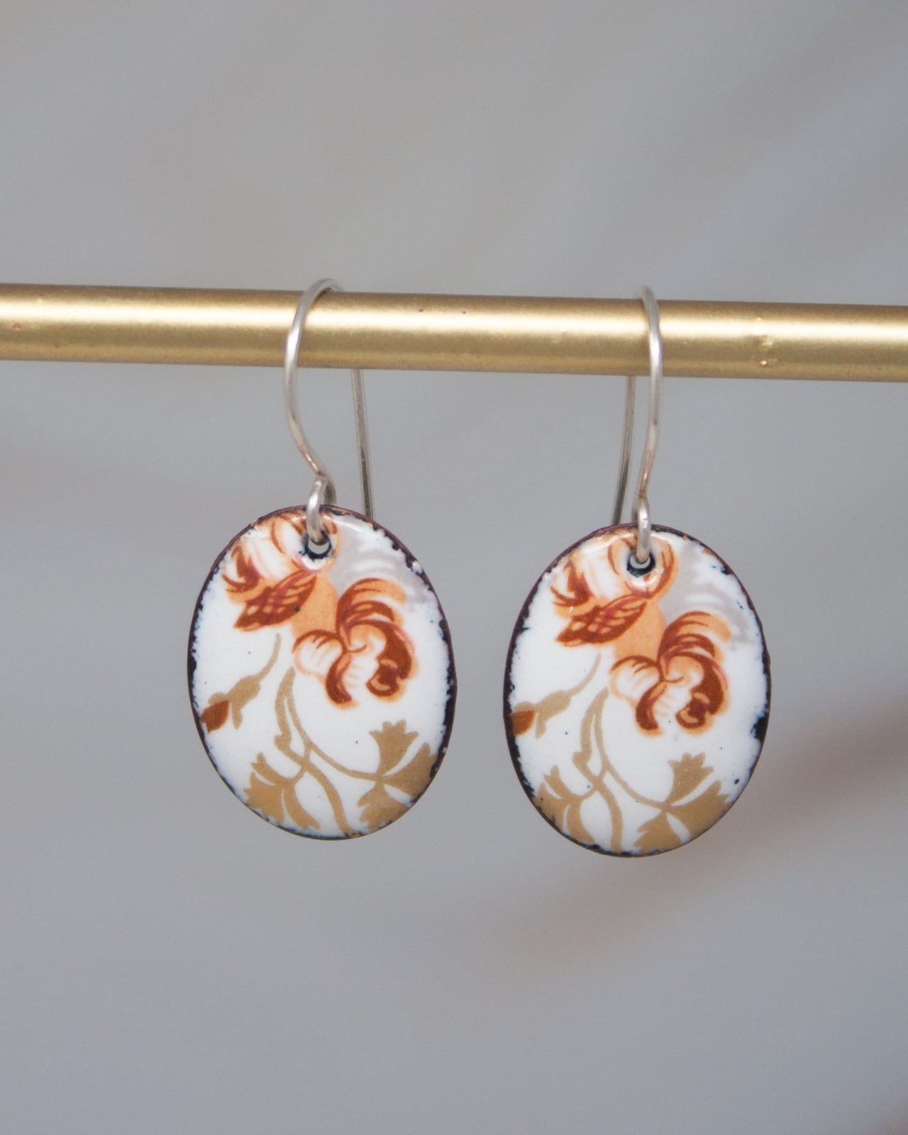 A pair of earrings with a floral design on a gold-colored metal bar.