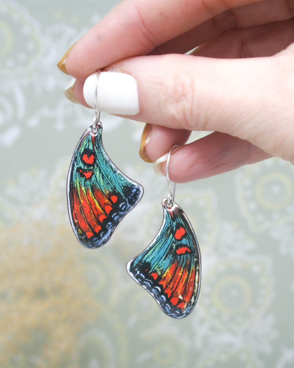 a hand holding a pair of colorful butterfly earrings