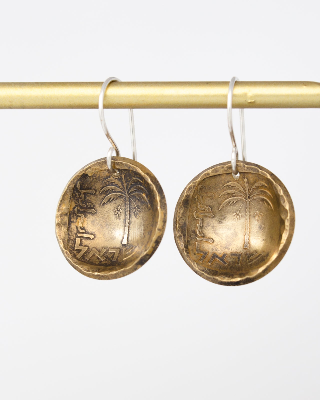 a pair of round, metallic earrings hanging from a gold-colored metal bar.