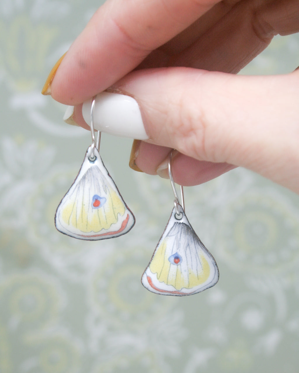 a hand holding a pair of tiny yellow and white earrings