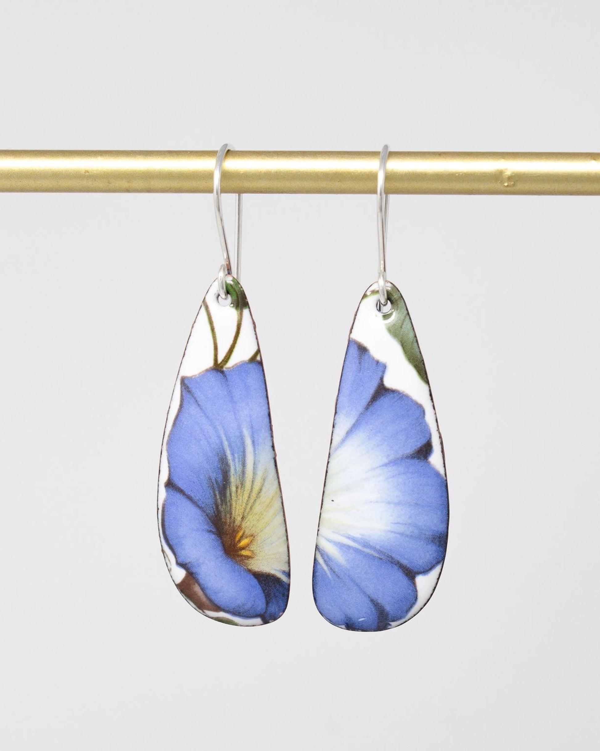 A pair of earrings with blue and white floral designs hanging from a gold bar.