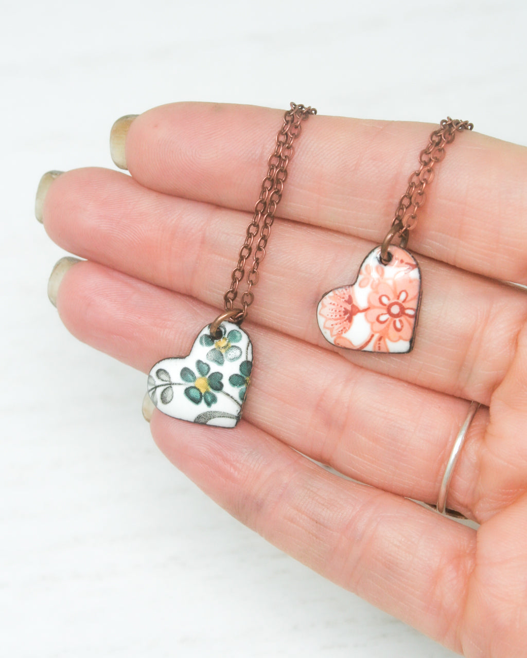 a hand holding two heart shaped pendants on a chain