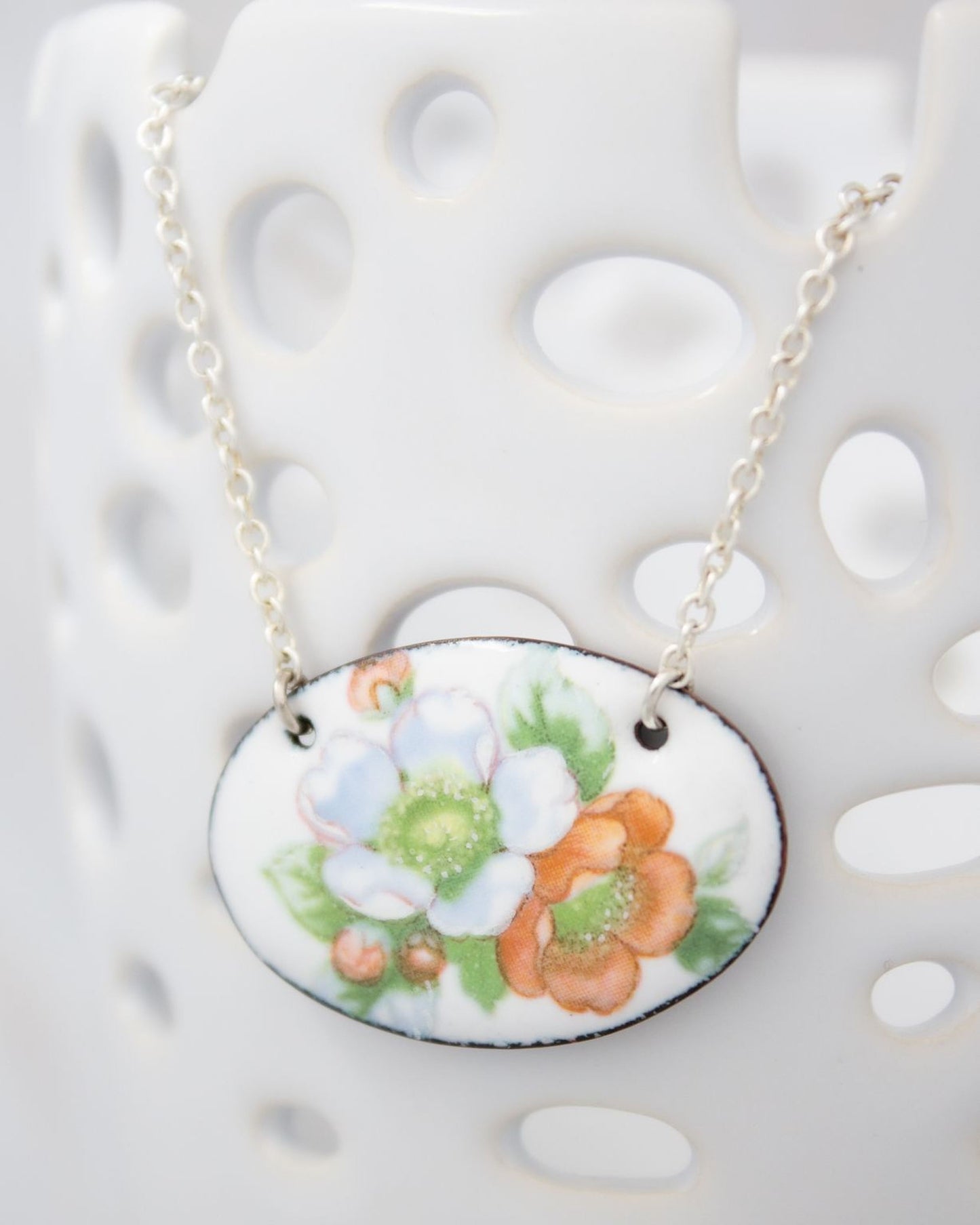 A necklace with a pendant featuring a floral design in white, orange, and green colors.