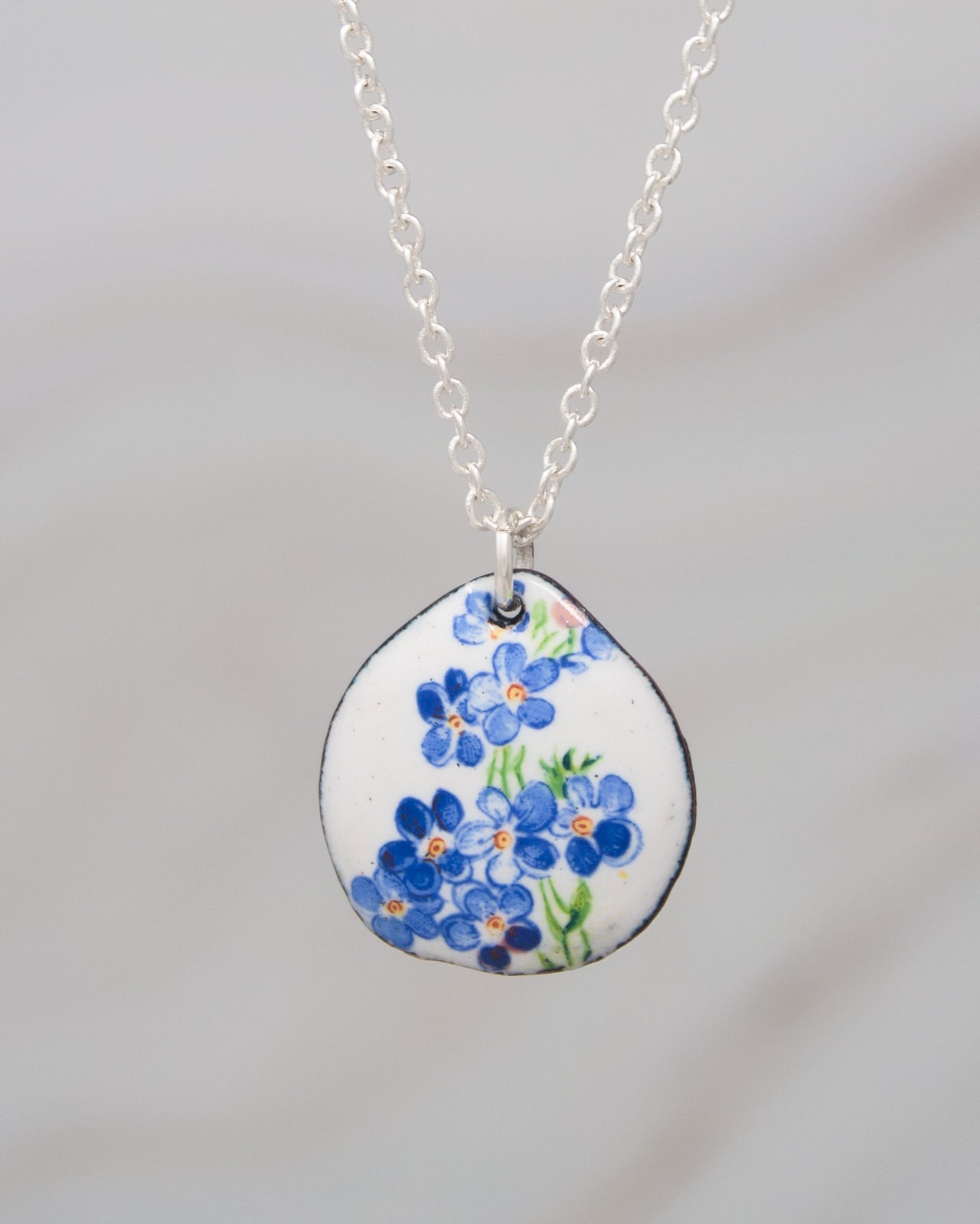 A silver necklace with a pendant featuring a blue flower design.