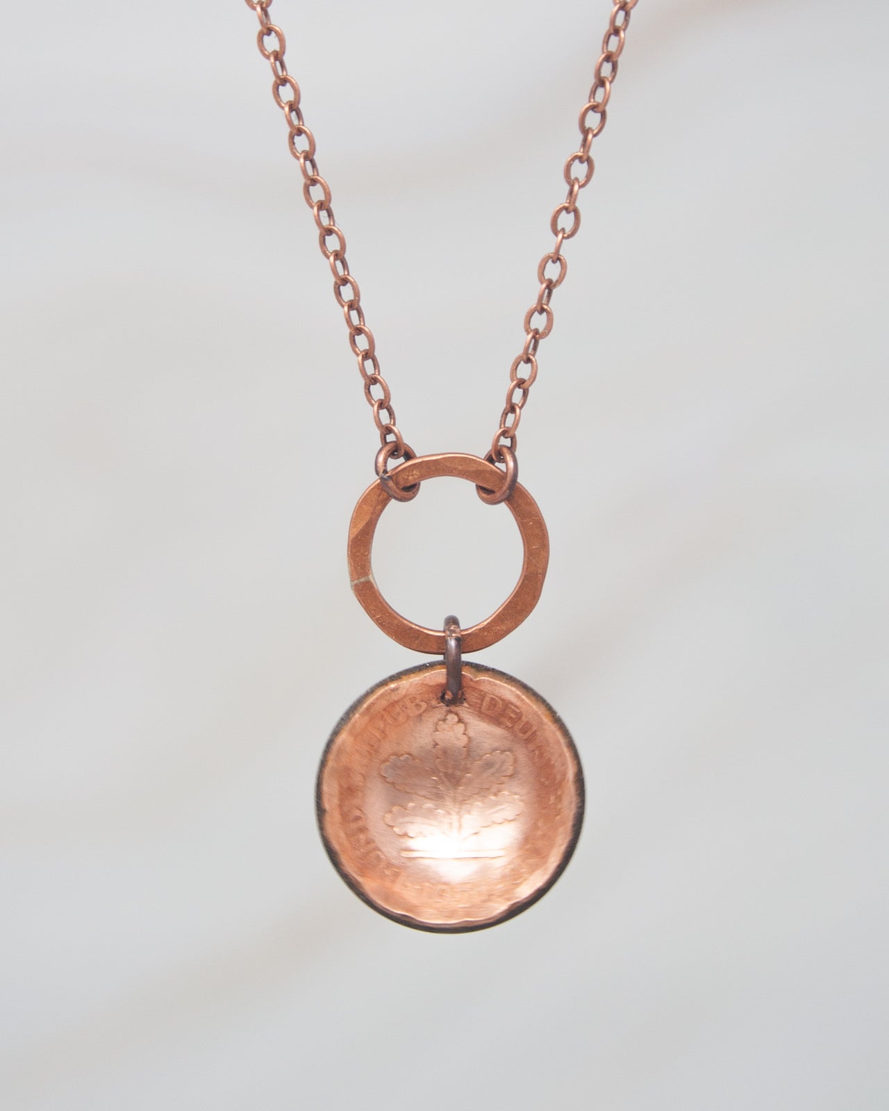 A copper-colored necklace with a circular pendant featuring an embossed design.