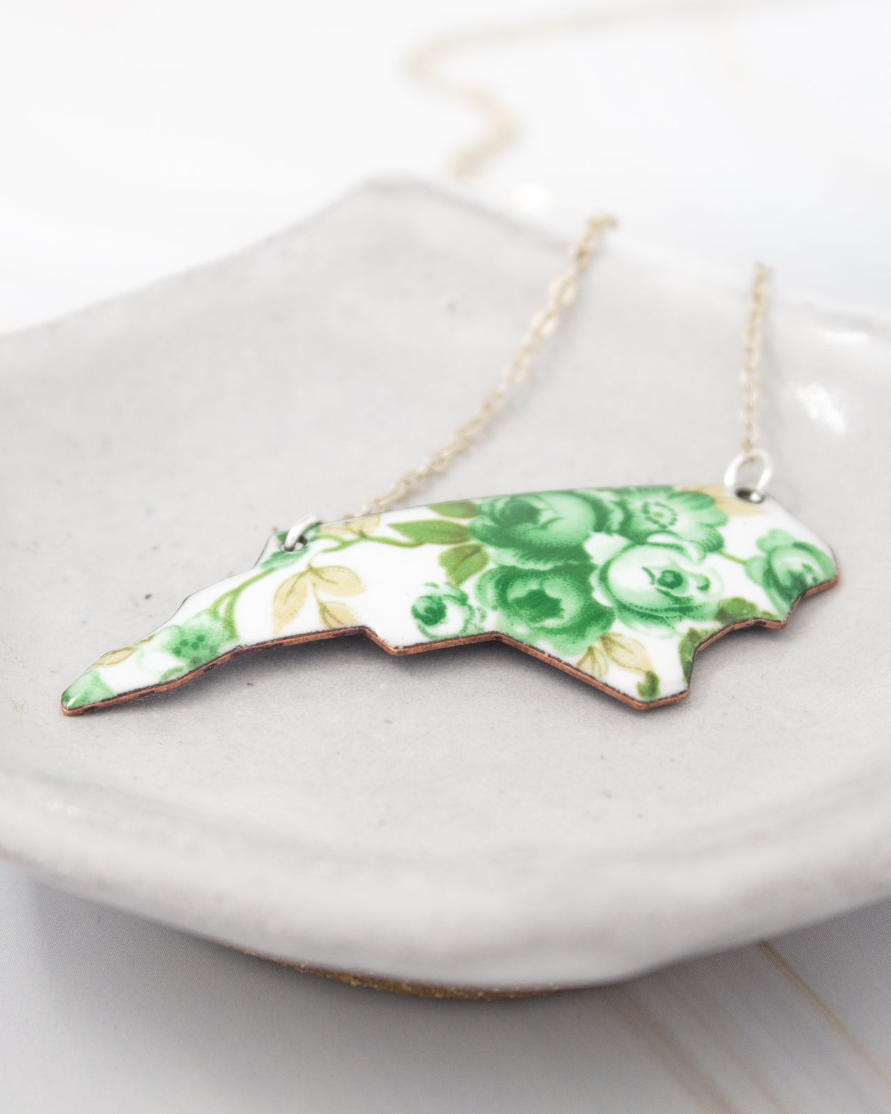 A necklace with a pendant in the shape of a flower, featuring green and white colors.