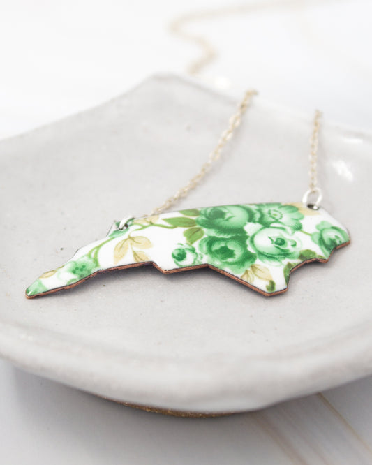 A necklace with a pendant in the shape of a flower, featuring green and white colors.