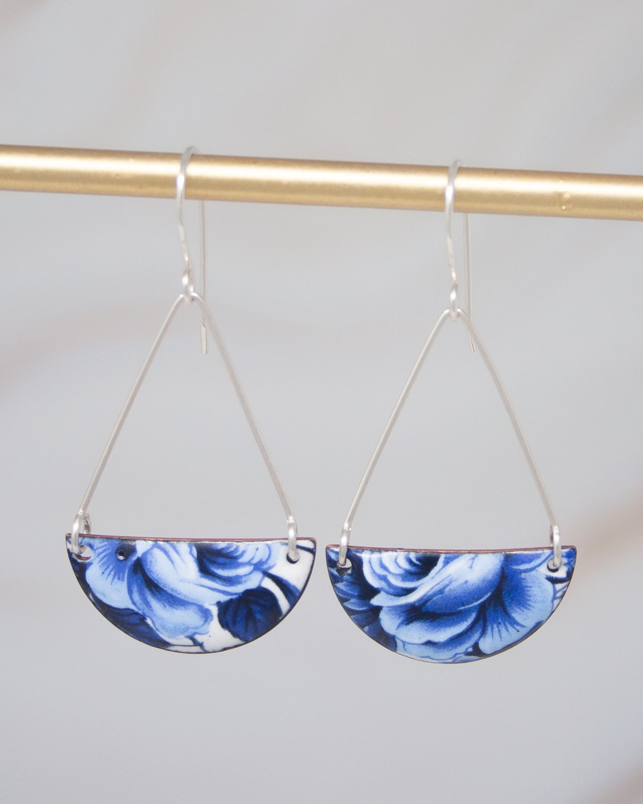 A pair of blue and white floral earrings hanging from a gold bar.