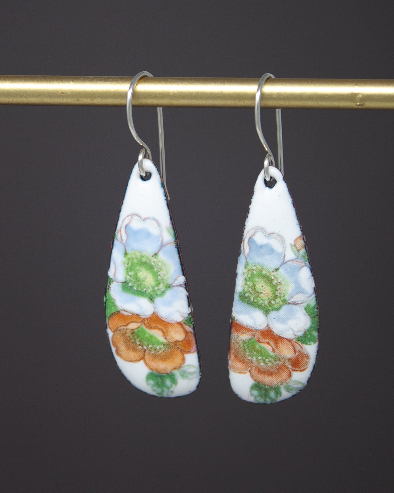 A pair of earrings with a floral design, hanging from a gold-colored metal hook.