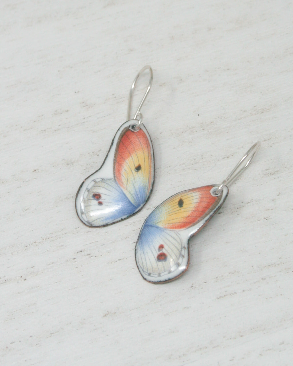 a pair of earrings with butterfly wing designs, resting on a white surface.