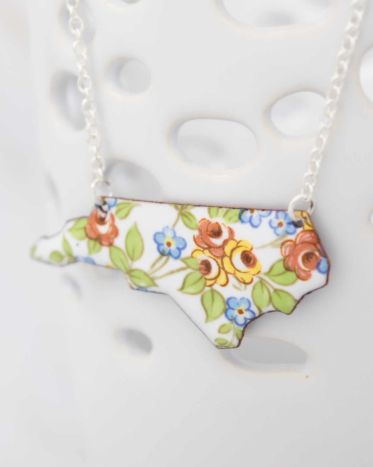 A necklace with a pendant in the shape of the state of North Carolina, featuring a floral design.