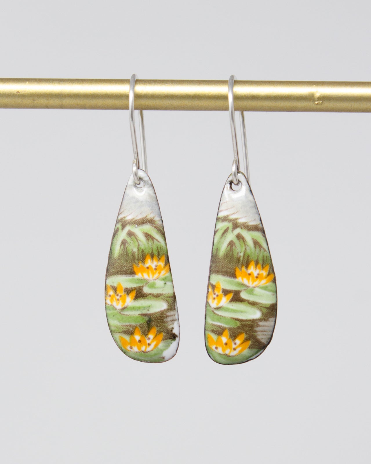 A pair of earrings with a floral design, featuring yellow flowers and green leaves, hanging from a gold-colored metal hook.