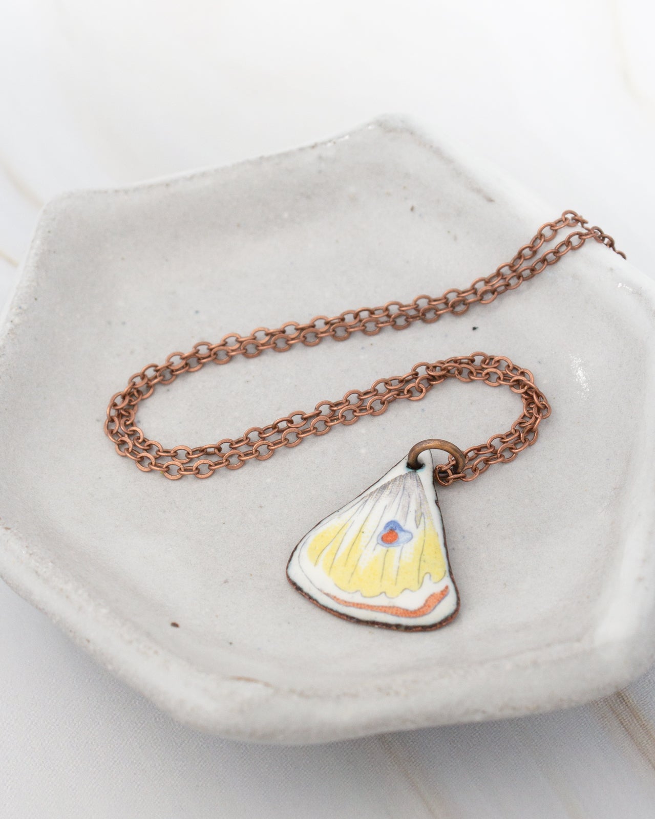 A necklace with a pendant featuring a yellow and orange design rests on a white plate.