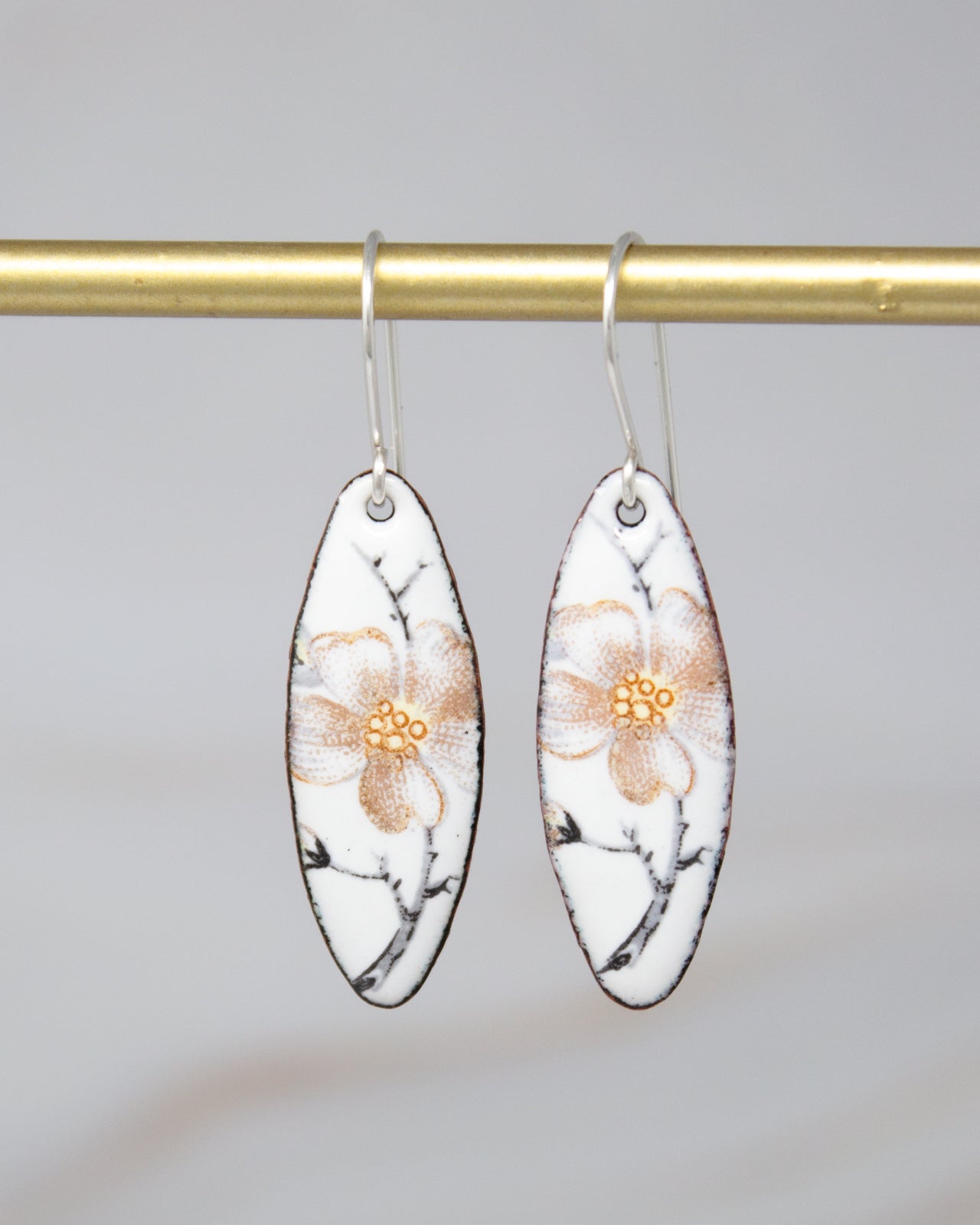 A pair of white earrings with a floral design hanging from a gold bar.