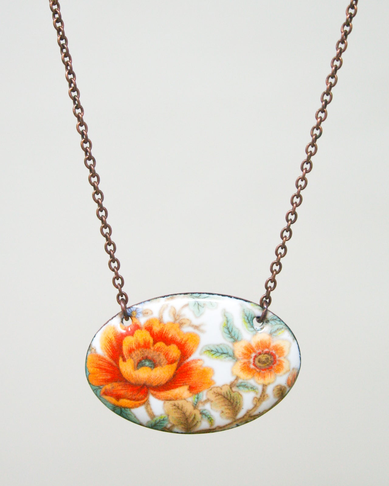 A necklace with a pendant featuring a floral design in shades of orange and white.