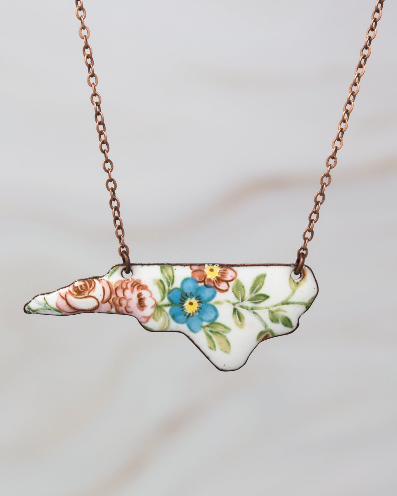 A necklace with a pendant in the shape of the state of North Carolina, featuring a floral design.