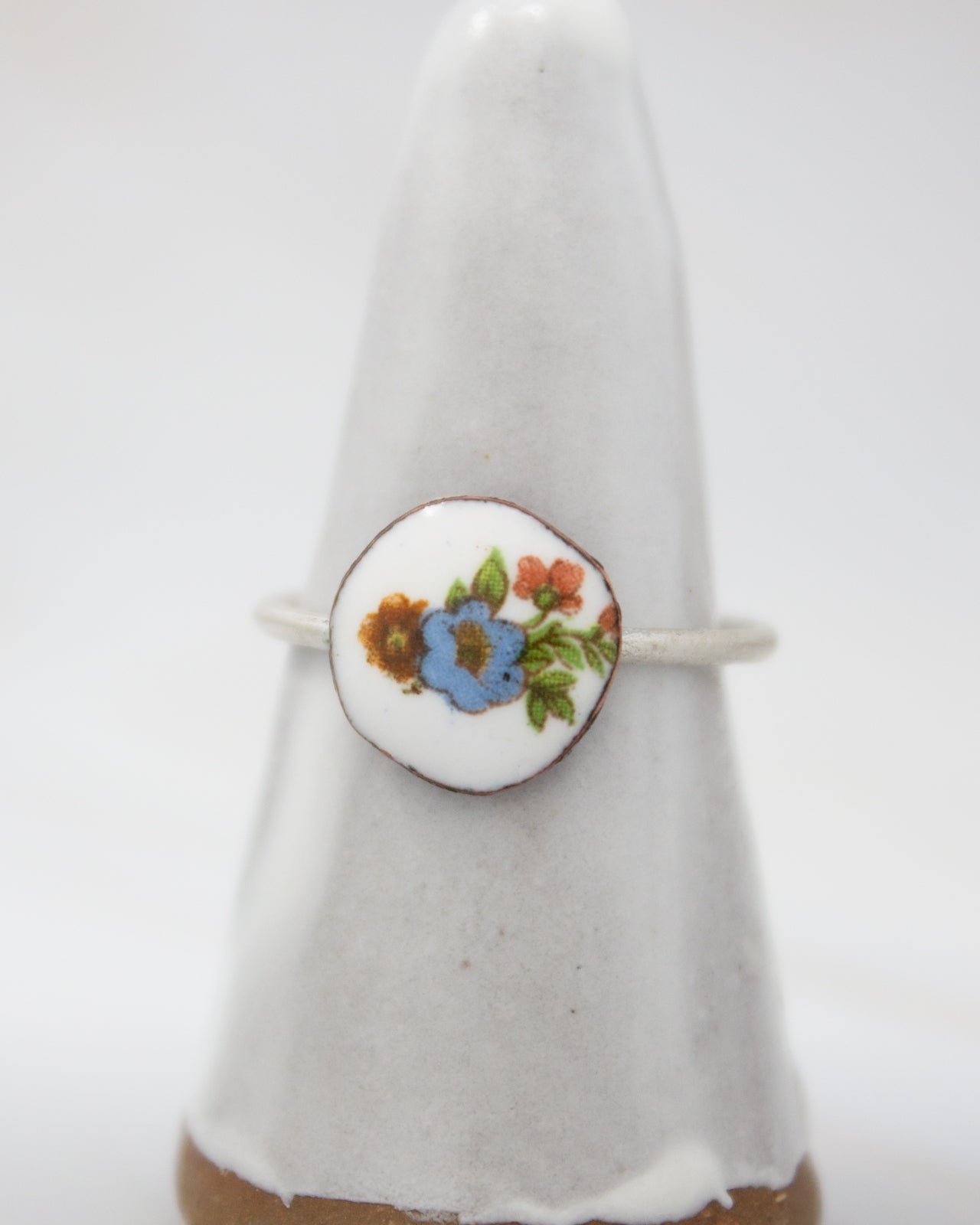A white ceramic ring with a floral design on it, placed on a white pedestal.