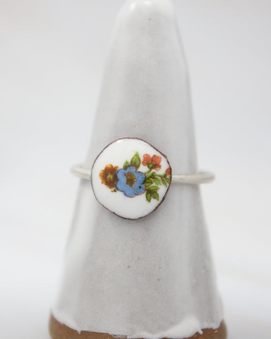 A white ceramic ring with a floral design on it, placed on a white pedestal.