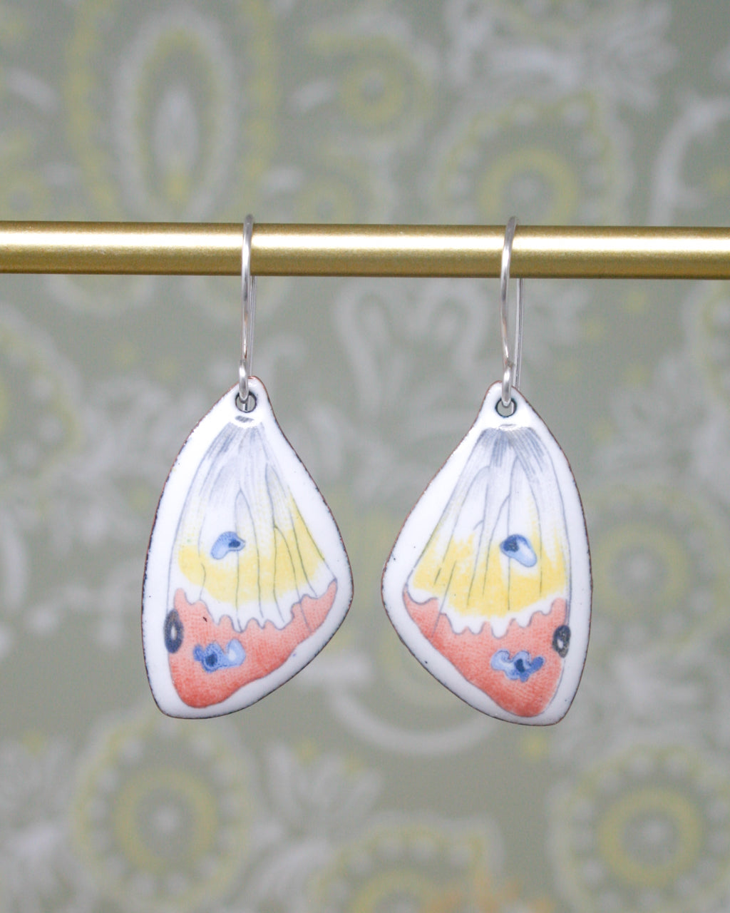 A pair of earrings with butterfly wing designs hanging from a gold-colored metal bar.