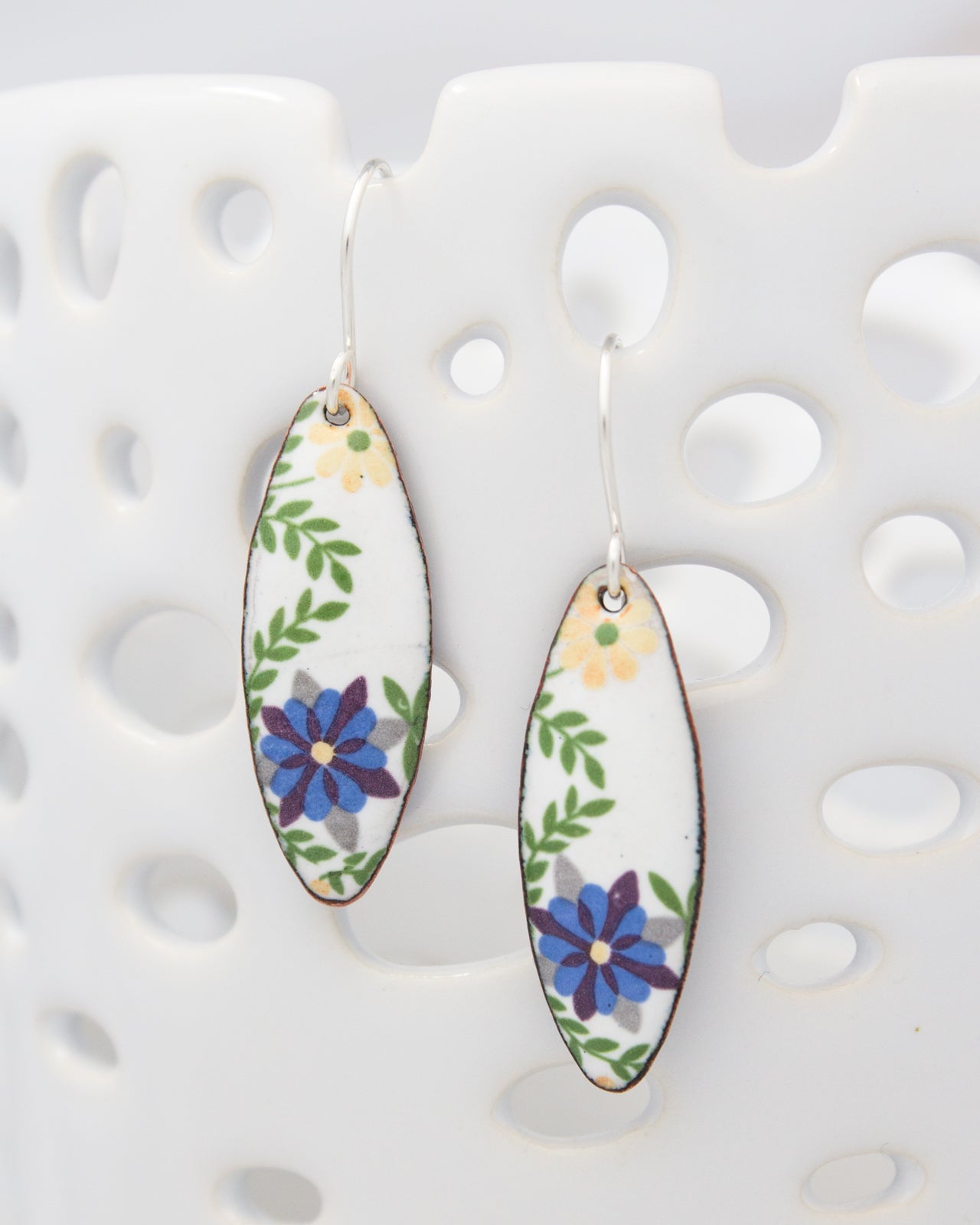 A pair of earrings with a floral design, featuring blue and purple flowers on a white background.