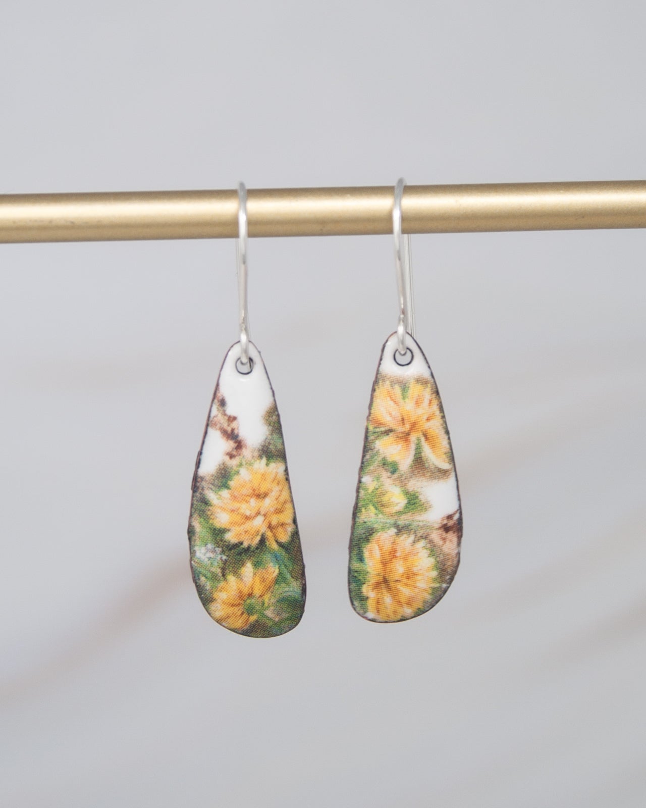 A pair of earrings with a floral design, featuring yellow flowers on a white background.